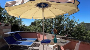 Eine Terrasse im Freien mit Tisch, Stühlen, Sonnenschirm und Liegestühlen.