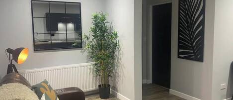 A modern living room with a brown leather sofa, a floor lamp, a potted plant, and a large mirror on the wall.