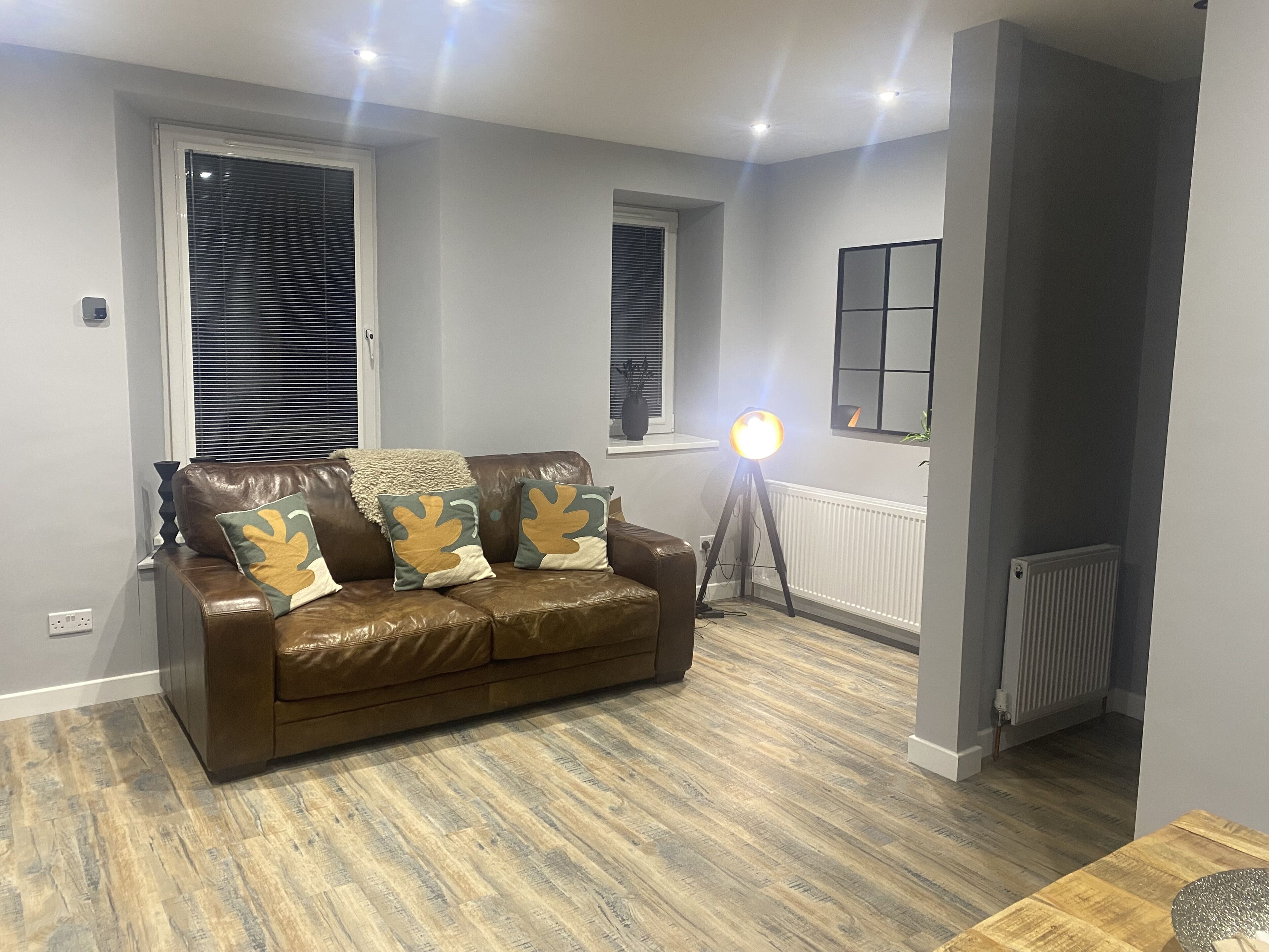 Un salon moderne avec un canapé en cuir marron, deux coussins assortis, une lampe sur pied et un radiateur.