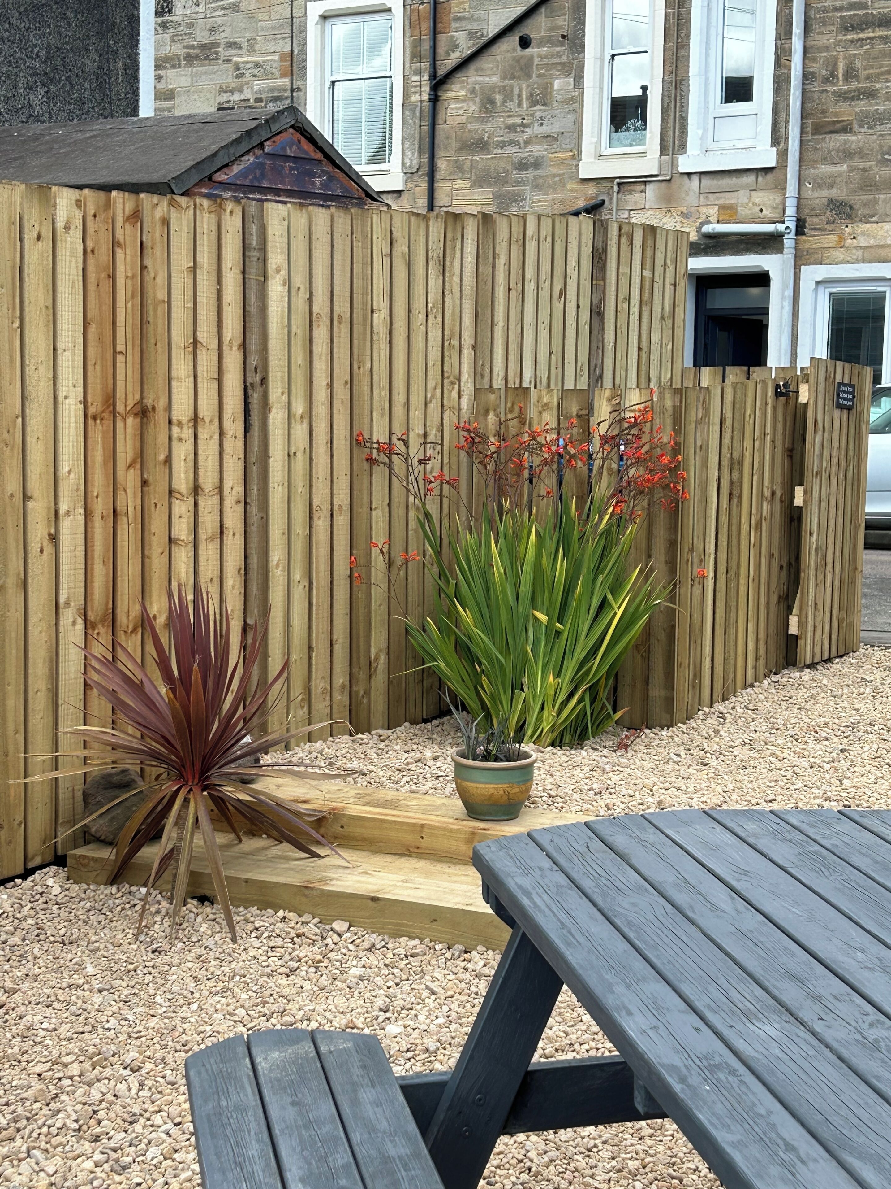 A wooden fence, a wooden table, and two potted plants in a garden area.