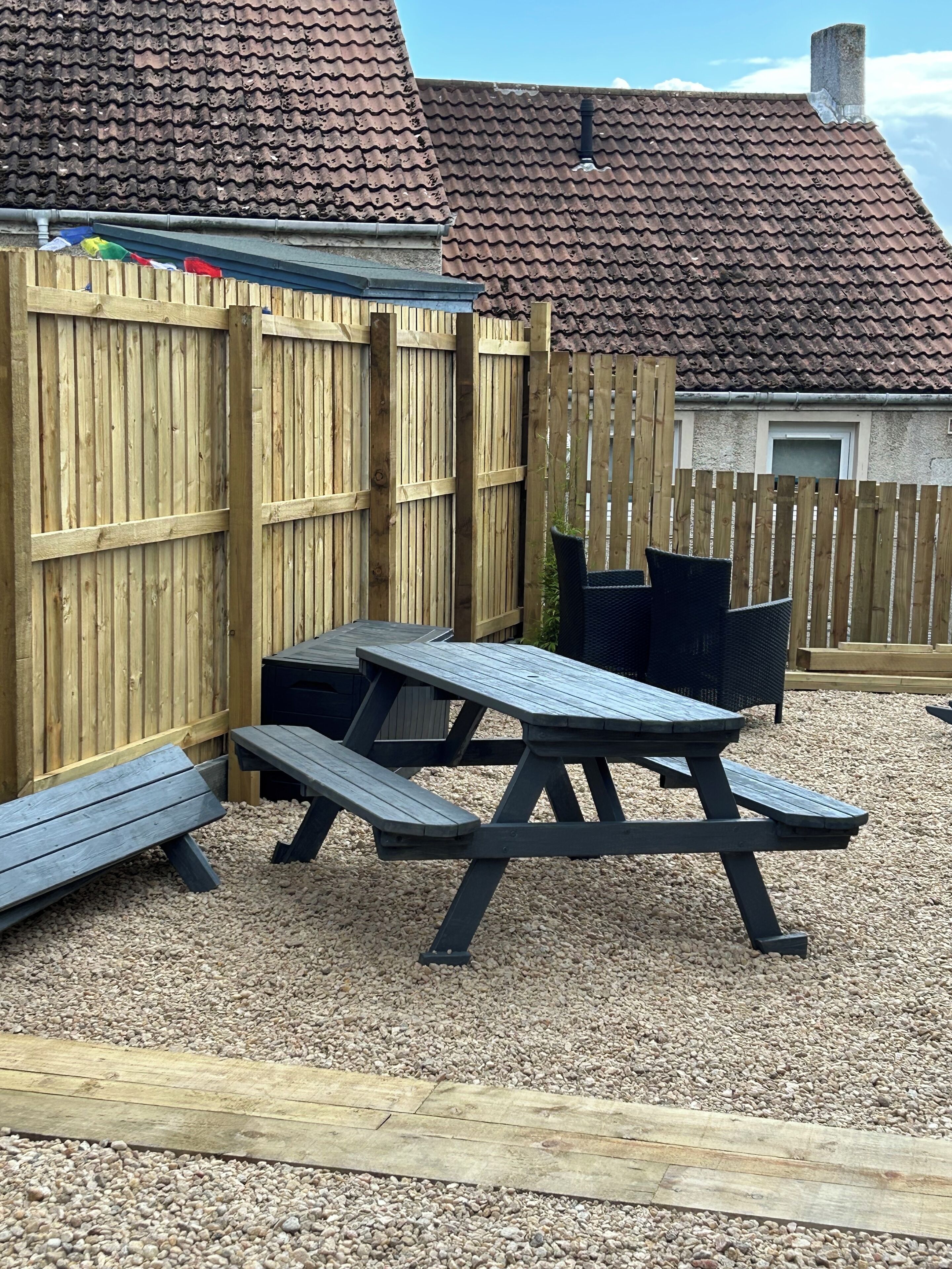A wooden picnic table with benches, surrounded by a wooden fence, set on gravel.