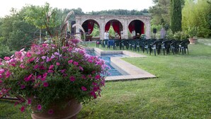 Un jardín con una estructura de ladrillo, una piscina y sillas dispuestas para un evento.