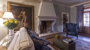 Una sala de estar con sofá, chimenea, un sillón azul y un cuadro en la pared.