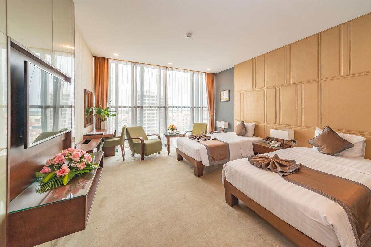 Habitación de hotel con dos camas, un escritorio, una silla, un televisor y vista a la ciudad.