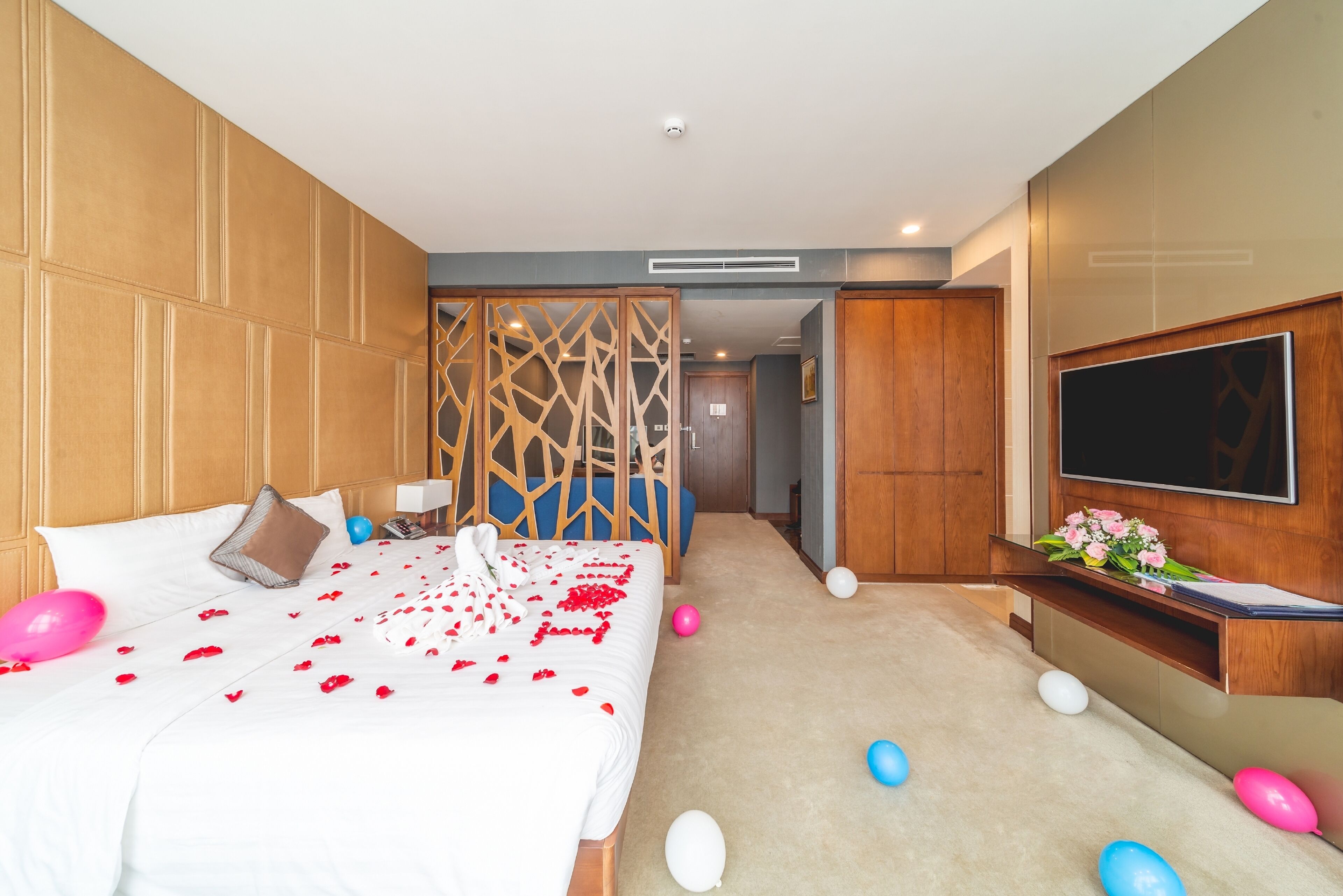 A hotel room with a large bed, a TV, and a desk with a flower arrangement.