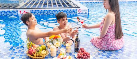 A poolside setting with a tiled floor, a pool, and a table with food and drinks.