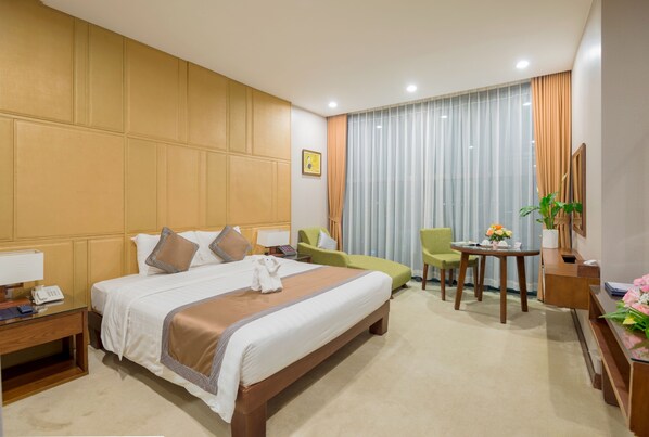 A hotel room with a large bed, a desk, a chair, a small table, and a window with curtains.