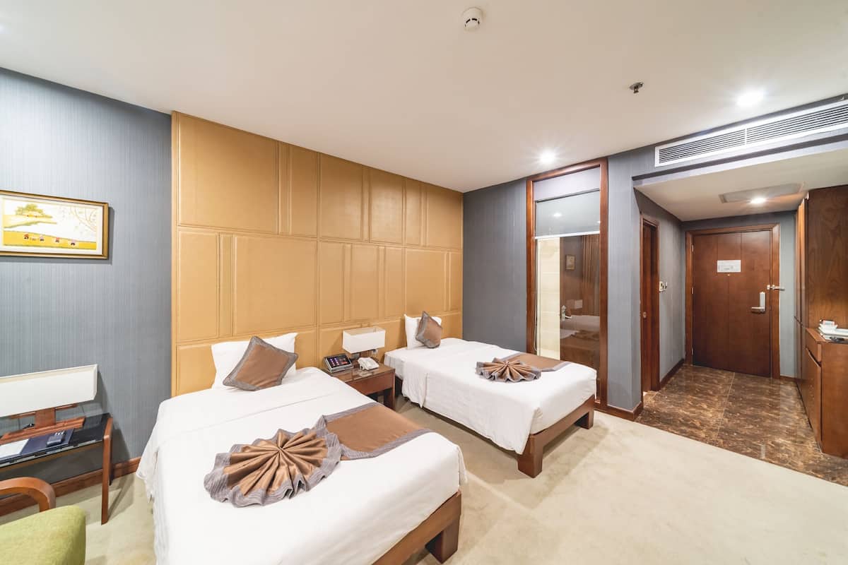 Habitación de hotel con dos camas, un escritorio, una silla y un baño visible a través de una puerta abierta.