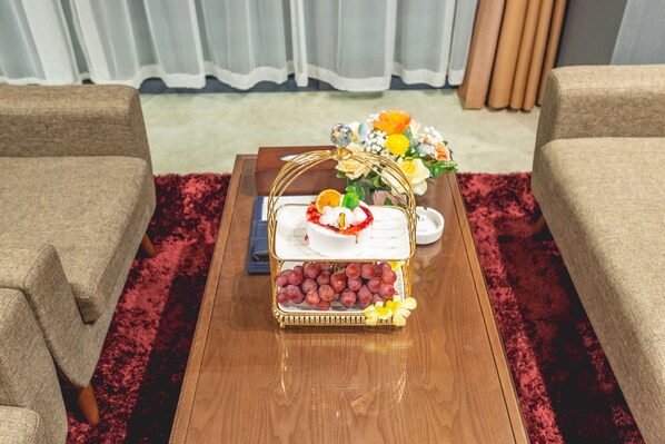 Una mesa de centro de madera con una composición de frutas, un florero y un control remoto.