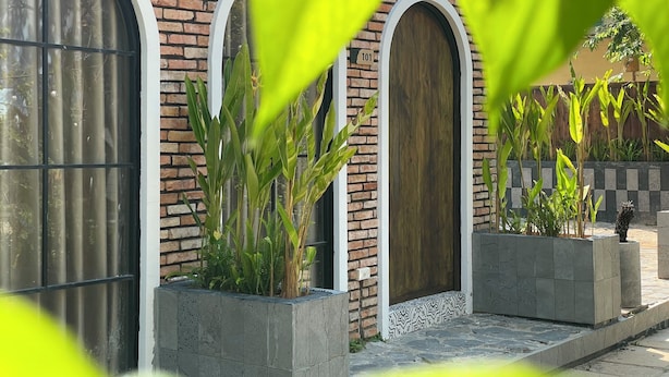 A building with arched windows and a wooden door, surrounded by potted plants and a brick wall. - Cottage Retreat DALAT (Cam Ly - Da Lat)