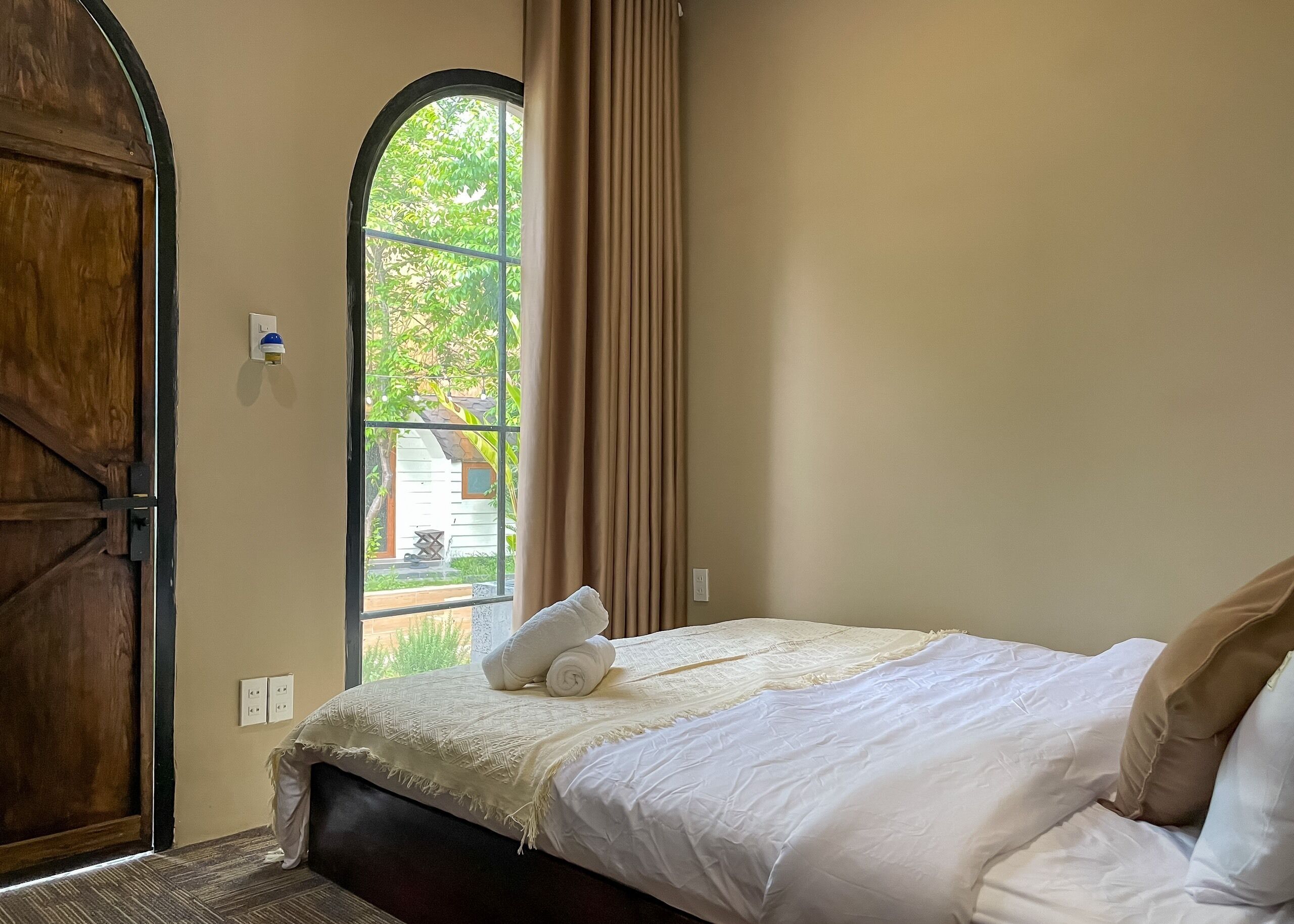 A bedroom with a large window, a bed with white linens, and a wooden door.