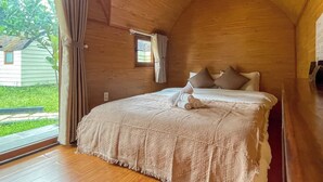 A cozy bedroom with a wooden ceiling, a bed with a patterned bedspread, two pillows, and a window with curtains. - Cottage Retreat DALAT (Cam Ly - Da Lat)