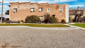 A two-story brick building with a flat roof, a small porch, and a gravel driveway. - Unique100 year old Historical Building Apt#2 (Ucon)