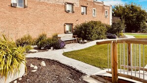 A brick building with multiple windows and a small garden area with a bench and potted plants. - Unique100 year old Historical Building Apt#2 (Ucon)
