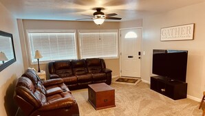 A living room with a brown leather sofa, a wooden coffee table, a television on a stand, and a ceiling fan. - Unique100 year old Historical Building Apt#2 (Ucon)