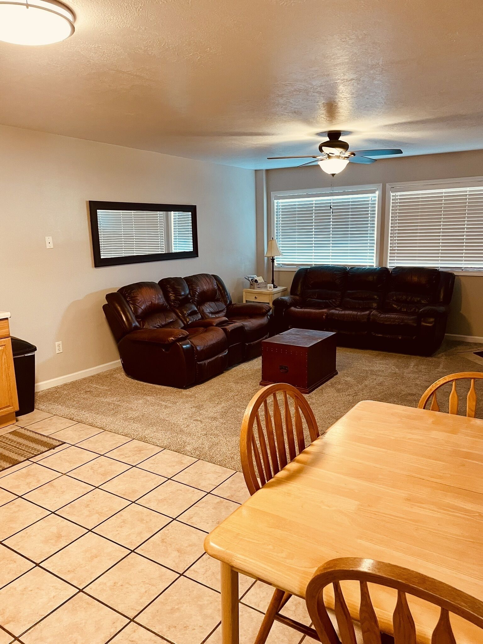 A living room with a brown leather sectional sofa, a wooden dining table with chairs, and a ceiling fan.