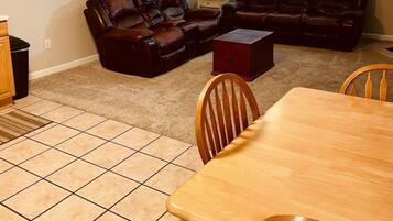 A living room with a brown leather sectional sofa, a wooden dining table with chairs, and a ceiling fan.