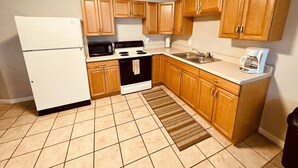 A compact kitchen with wooden cabinets, a white refrigerator, a stove, a microwave, and a coffee maker. - Unique100 year old Historical Building Apt#2 (Ucon)