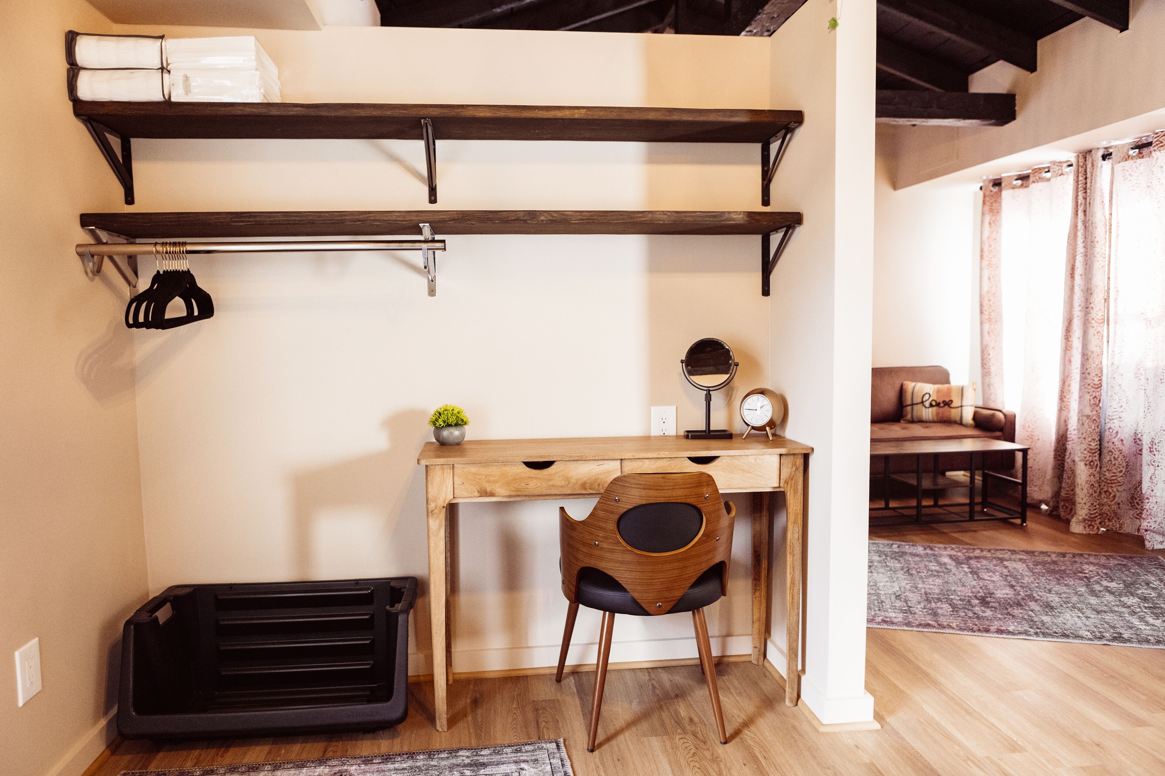 Une pièce de taille modeste, comprenant un bureau en bois, une chaise, une poubelle noire et une petite plante en pot.