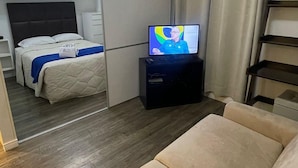 Uma sala de estar moderna com sofá, televisão, cama com manta azul e porta deslizante para um quarto.