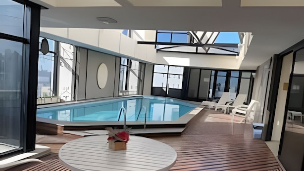 Uma área interna de piscina moderna, com mesa de bilhar, cadeiras de descanso e grandes janelas com vista para a cidade.