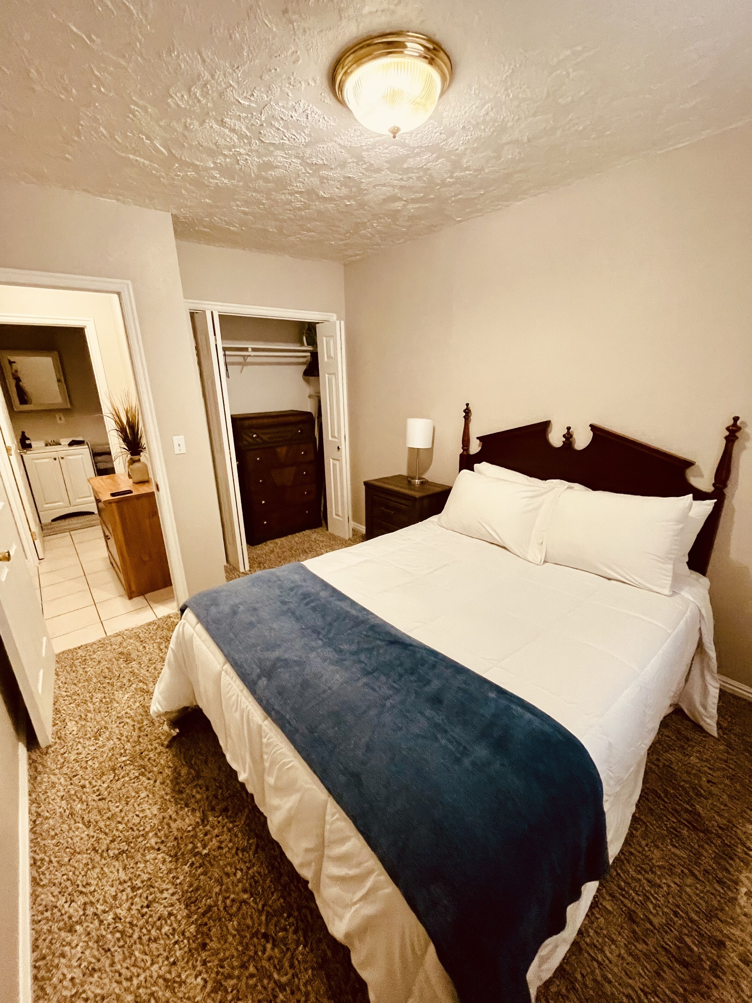 Un dormitorio con una cama grande, una mesita de noche, un aparador y una lámpara de techo.