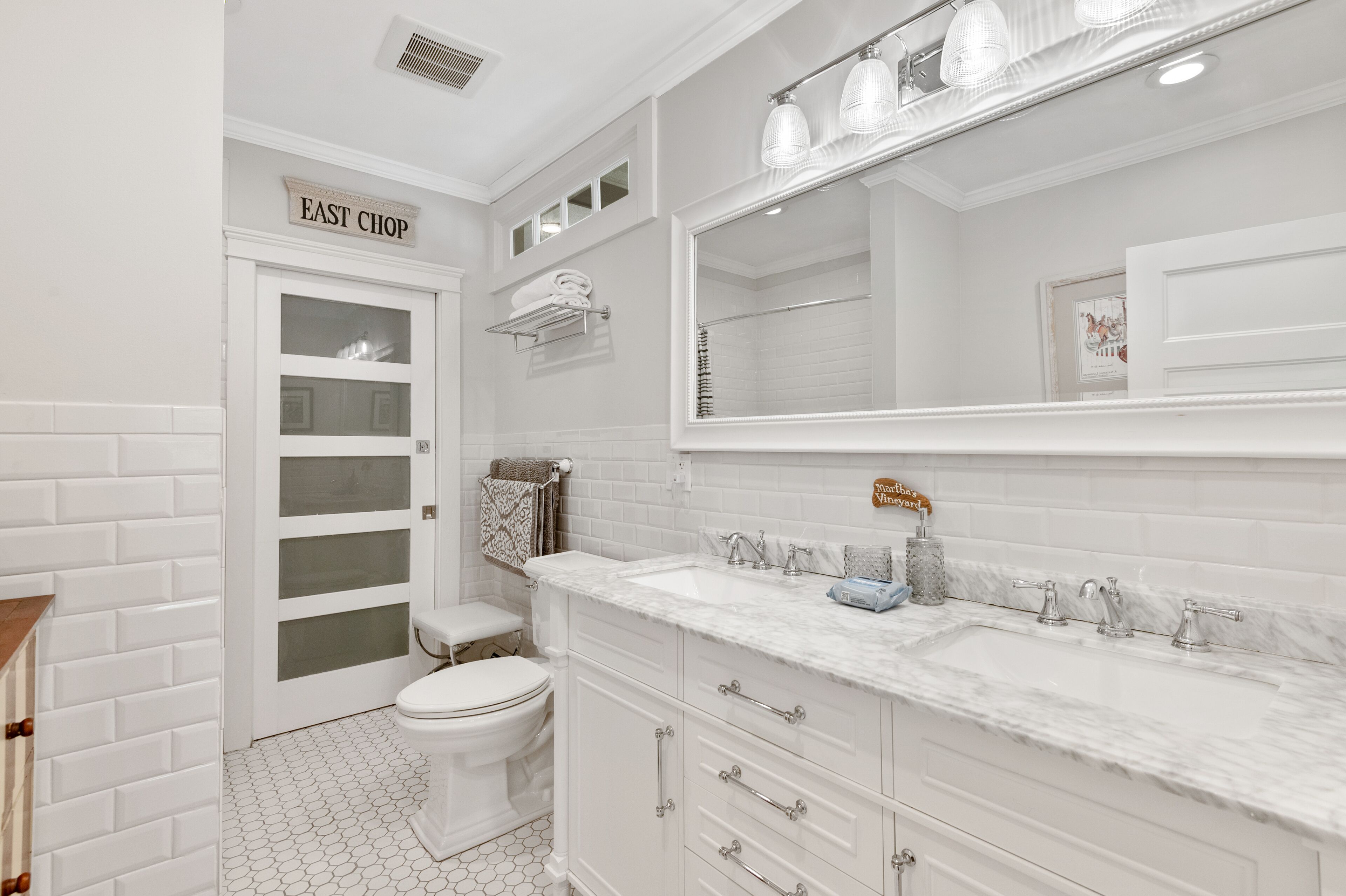 Un baño con inodoro blanco, lavabo con encimera de mármol y un espejo grande sobre el lavabo.