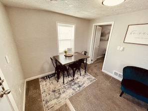 A dining area with a table and chairs, a rug, and a framed sign on the wall. - Small Group Apartment in Century-Old Building Apt#4 (Ucon)