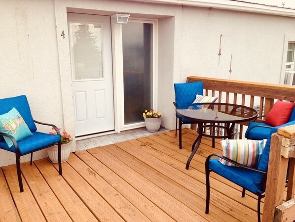 A wooden deck with a white door, two blue chairs, a round table, and a wooden bench. - Small Group Apartment in Century-Old Building Apt#4 (Ucon)