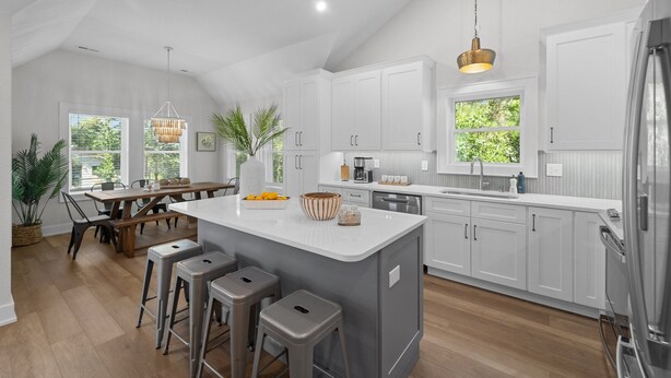 A modern kitchen with white cabinetry, a large island with stools, and a stainless steel refrigerator.