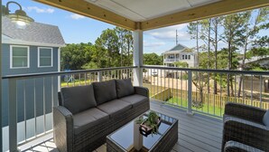 A covered porch with a wicker sofa and a glass coffee table, overlooking a backyard with a wooden fence and trees.
