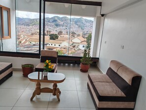 A balcony with a view of a cityscape, a wooden table, a brown sofa, and two potted plants. - Paqarina san Blas (Cusco)