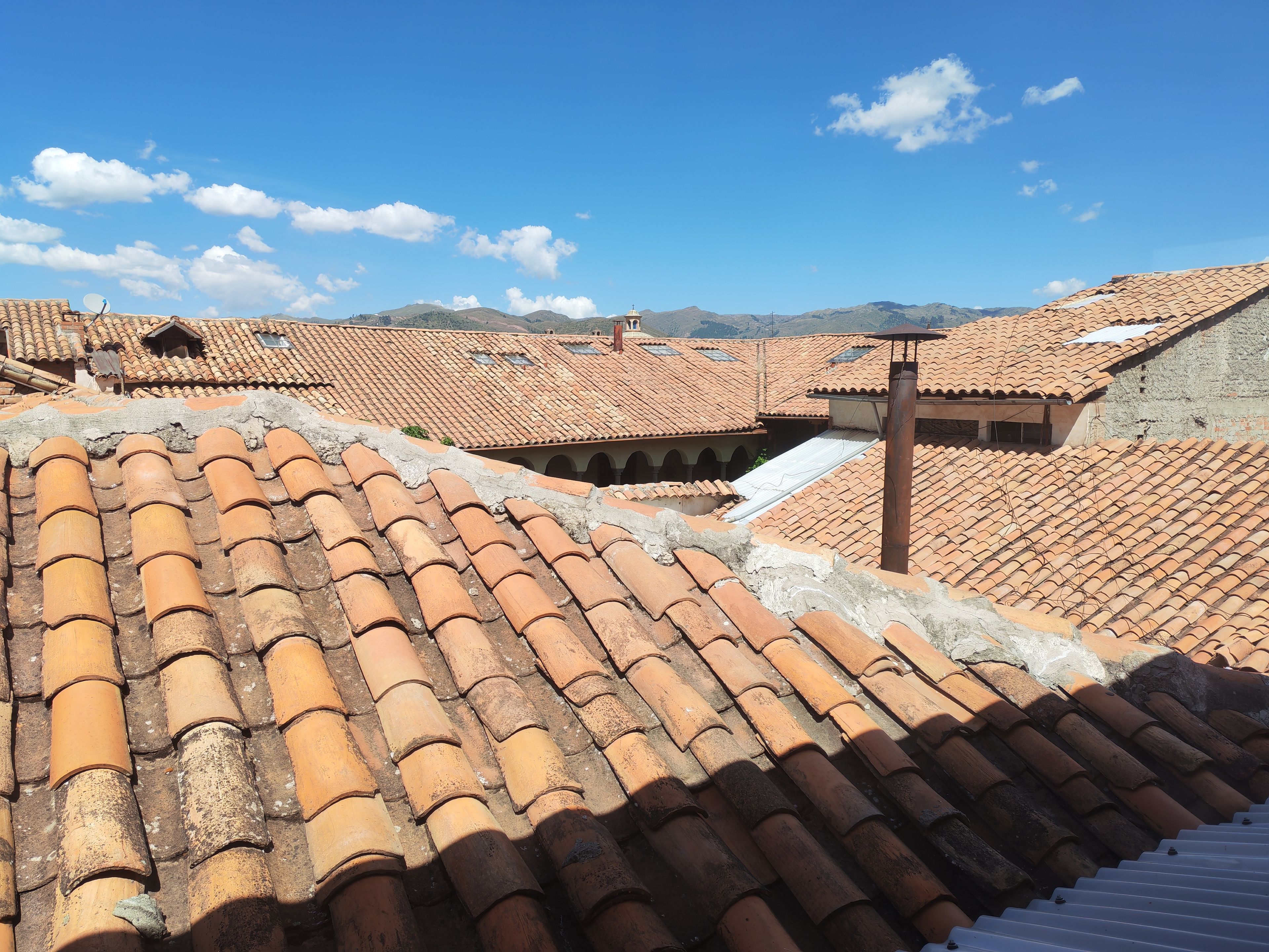 Una azotea con tejas de terracota, una antena parabólica y vistas a montañas distantes.