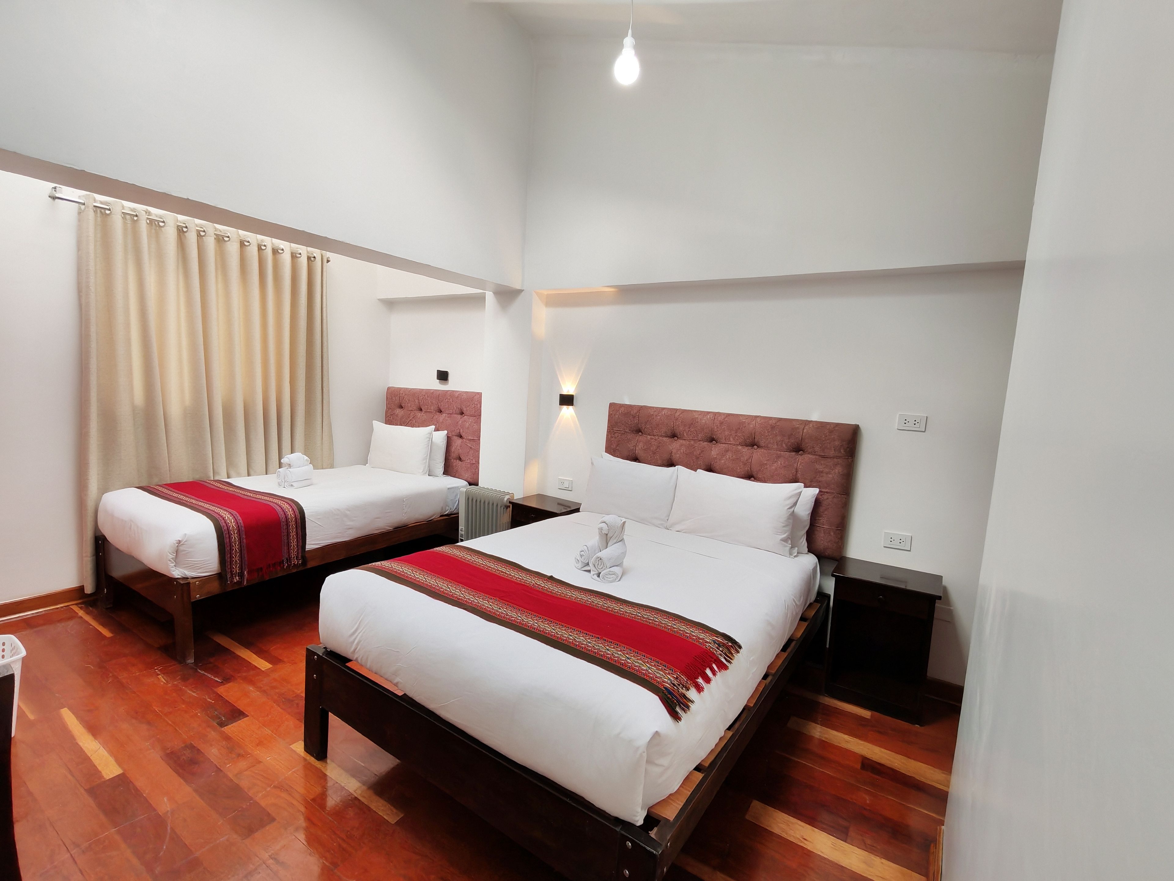 Quarto de hotel com duas camas, piso de madeira e janela com cortinas.