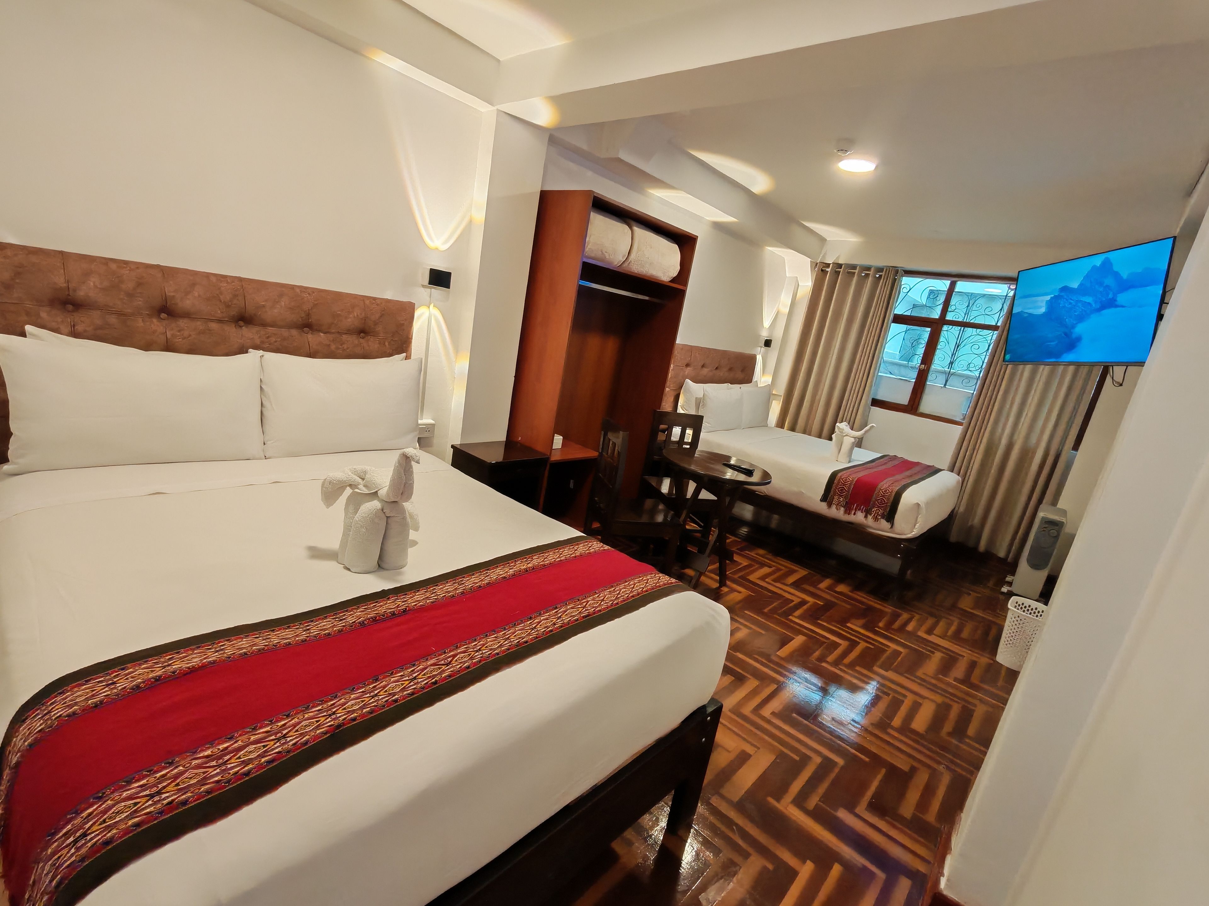A hotel room with a large bed, a smaller bed, a desk, a chair, a TV, and a wardrobe.