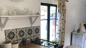 A kitchen with a gas stove, white cabinets, patterned backsplash, and a window with curtains. - Kouzelná maringotka (Chribska)