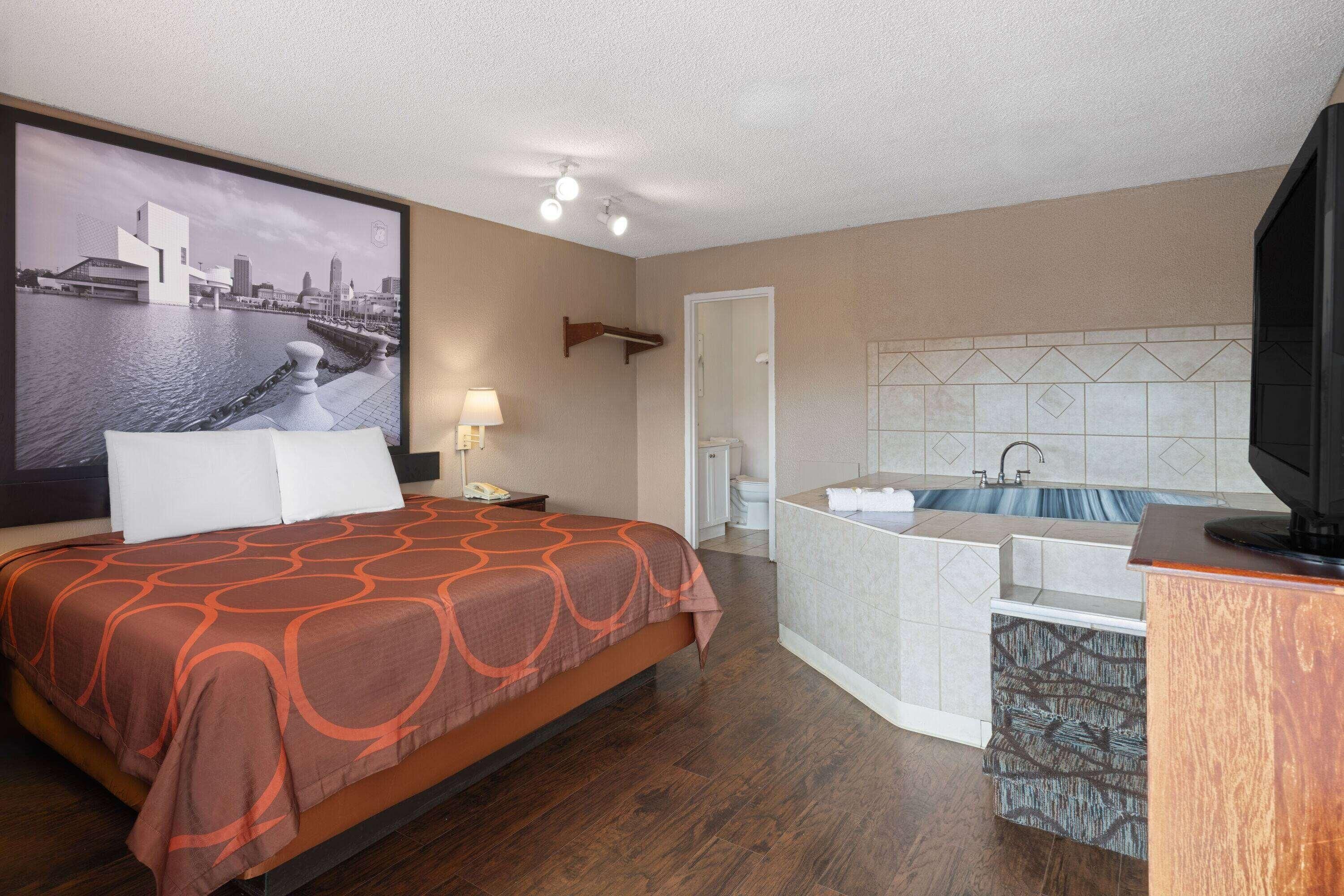A hotel room with a bed, a bathroom with a bathtub, and a large window with a cityscape view.