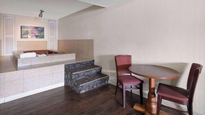 Quarto de hotel com um banco de padrão de pedra, uma mesa de madeira redonda e duas cadeiras vermelhas.