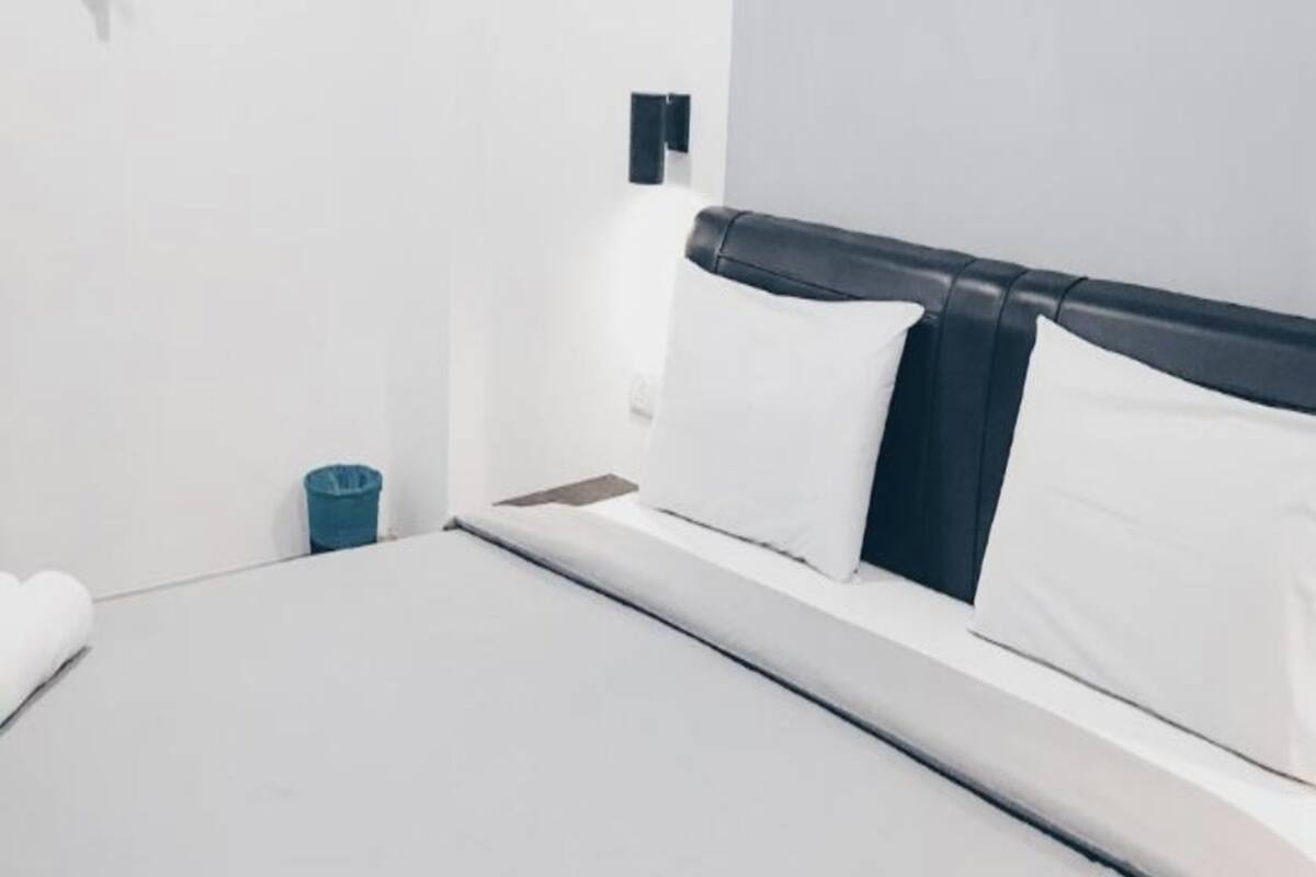 A hotel room with a bed, white walls, a blue trash bin, and a black headboard.