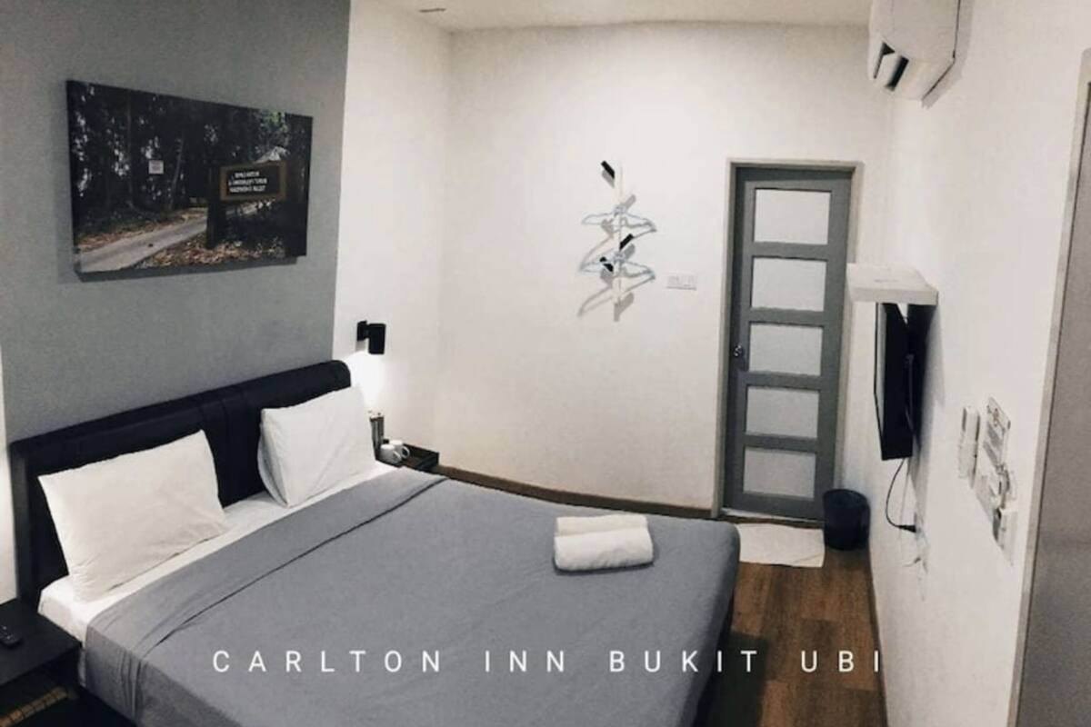 A hotel room with a bed, a nightstand, a wall-mounted TV, and a door.