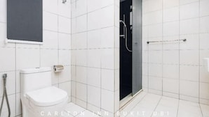 A modern bathroom with white tiles, a toilet, a shower area, and a glass door. - OYO 89492 Carlton Inn Bukit Ubi (Kuantan)