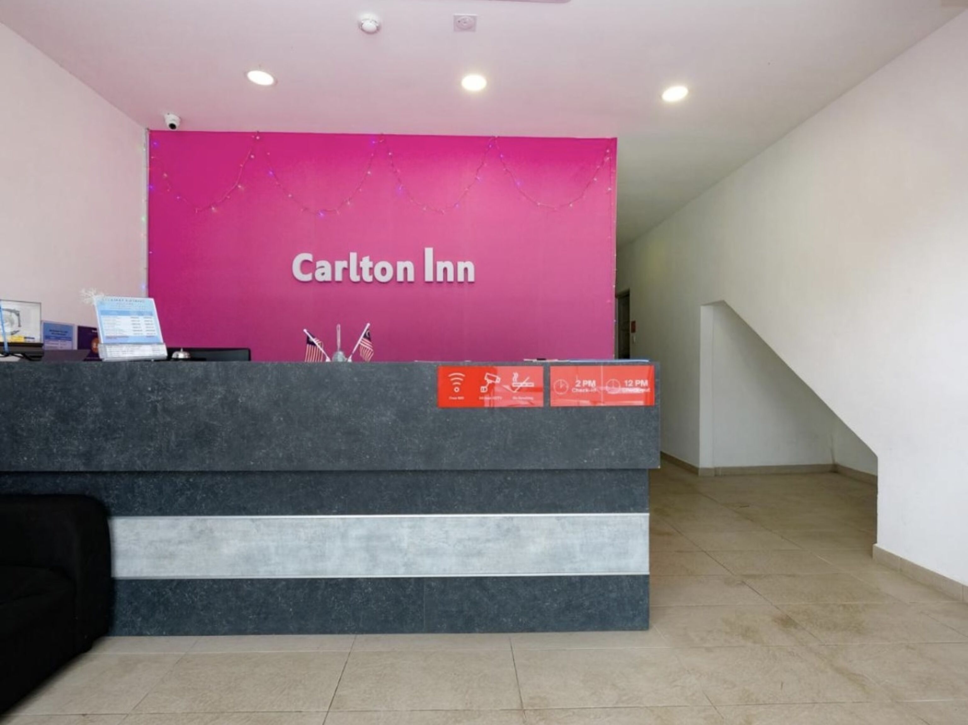 Una reception del Carlton Inn con una parete rosa, un computer e un cartello che indica gli orari di check-in.