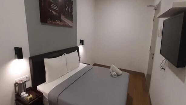 A hotel room with a bed, nightstand, lamp, and a flat-screen TV mounted on the wall. - OYO 89492 Carlton Inn Bukit Ubi (Kuantan)