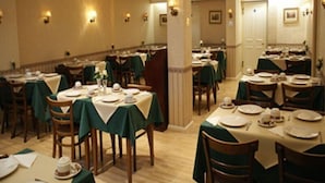 A formal dining room with multiple tables set for service, featuring green tablecloths and white table settings.