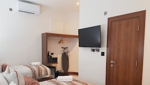 A hotel room with two beds, a flat-screen TV mounted on the wall, a wooden door, and a small desk with a coffee maker and ironing board.