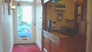 A hallway with a red carpet leading to a reception area with a wooden desk and a computer monitor.