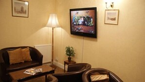A living room with a sofa, two armchairs, a coffee table, a floor lamp, a television, and a small table with a plant.