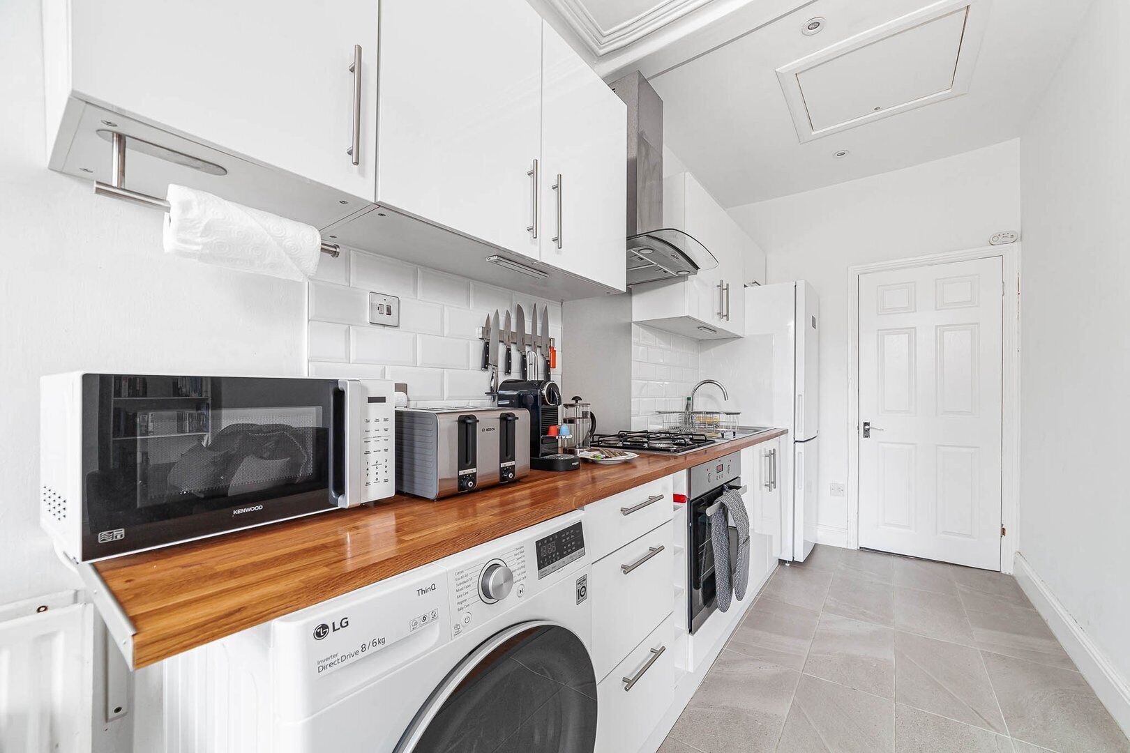 Une cuisine moderne avec des meubles blancs, un four à micro-ondes, un grille-pain, une machine à café et un lave-linge.