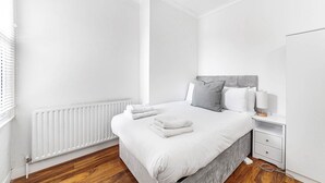 A modern bedroom with a large bed, white walls, and a wooden floor.