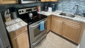 A kitchen with wooden cabinets, a stainless steel stove, a microwave, and a tiled backsplash.